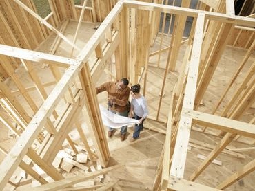 Two construction workers reviewing blueprints inside a timber-framed residential build